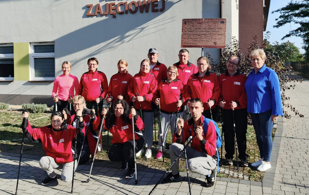 Grupa os&oacute;b w strojach sportowych i z kijkami przed budynkiem WTZ
